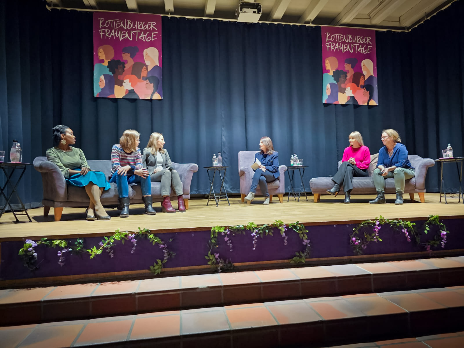 Mehrere Frauen diskutieren miteinander auf einem Podium