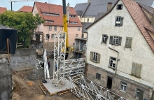 Kranteile liegen auf dem Boden in einem Hinterhof. Eines davon wird von einem anderen Kran angehoben.