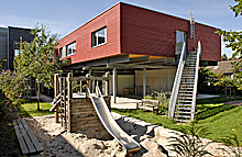 Sandkasten und Spielgeräte vor modernem Gebäude