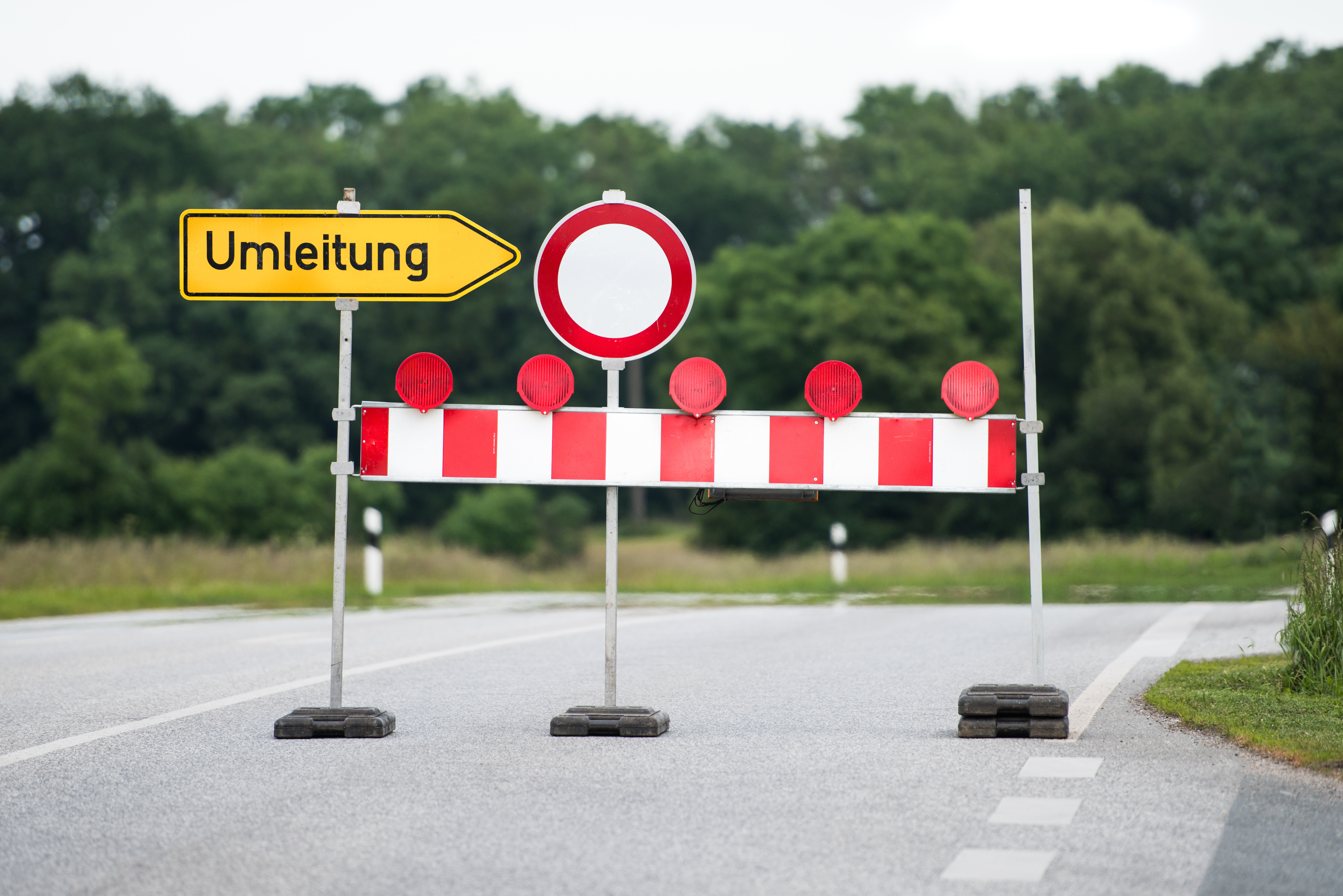 Eine orangene Absperrung, die die Durchfahrt auf einer Straße verhindert.