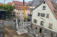 Kranteile liegen auf dem Boden in einem Hinterhof. Eines davon wird von einem anderen Kran angehoben. 