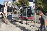 Ein kleiner Bagger am Bahnhof mit einem Bauarbeiter im Profil davor. 