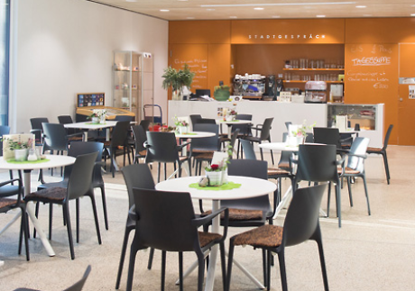 Innenansicht eines Cafés mit gedeckten Tischen und Stühlen, sowie einer Bedientheke. Quelle: Café Stadtgespräch