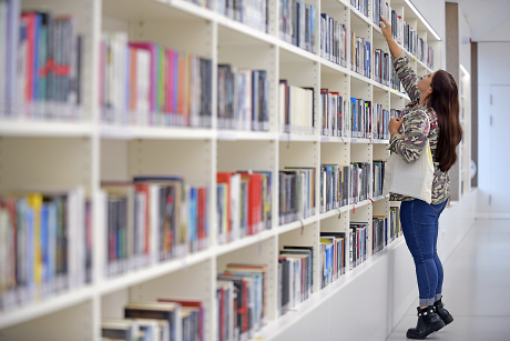 Junge Frau an einem Bücherregal, sie greift ins obere Regalfach Quelle: Steffen Schlüter