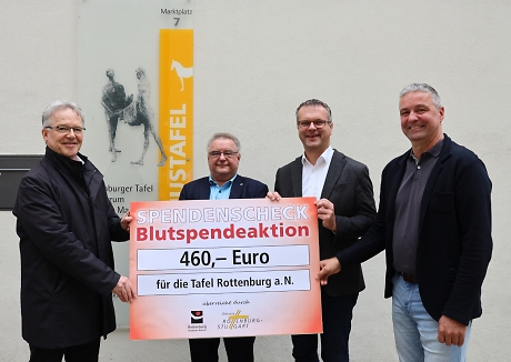 Vier Männer halten einen großen Spendenscheck und lächeln in die Kamera.