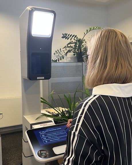 Frau steht mit dem Rücken zum Betrachter vor einem Fotoaufnahmegerät im Bürgerbüro