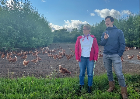 Zwei Personen auf einer Wiese vor einem Hühnergehege.
