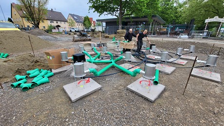 Ein Wasserspielplatz wir gebaut. Der Boden ist mit Kies gefüllt, es schauen Schläuche heraus.