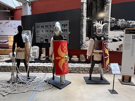 Drei nebeneinander stehende Statuen von römischen Gladiatoren mit Rüstung im Innenraum eines Museums.