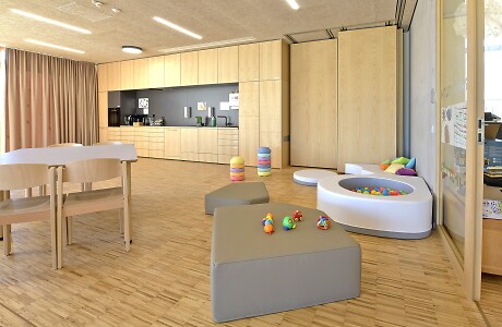 Der Gemeinschaftsraum des Kinder- und Familienzentrums mit einer offenen Küche, einigen Tischen und Stühlen, einem Bällebad und Spielsachen.