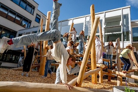 Ein Mädchen macht vor einem Klettergerüst einen Handstand auf dem Pausenhof