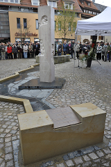 Brunnenanlage und mit herausgearbeiteten Bilddarstellungen gestaltete Steinsäule.