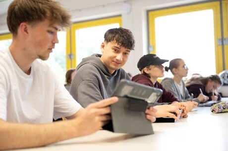 Schüler sitzen am Schreibtisch und schauen gemeinsam in ein Tablet-PC