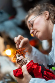 Eine Puppenbauerin, die eine kleine, rote Puppe näht
