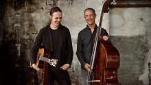 Zwei Musiker, lachend. Der linke ist Aleksi Rajala mit der Gitarre unter dem Arm und der rechte ist Florian Dohrmann am Kontrabass